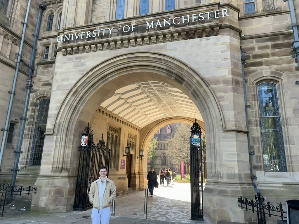 Aaron Gold standing under the University of Manchester archway
